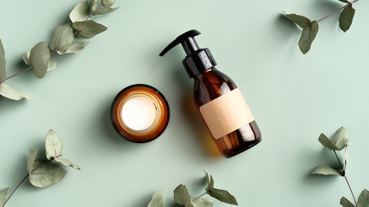 Skincare Cosmetics Products and Eucalyptus Leaves on Green Background Top View. Flat Lay Jar of Moisturizer Cream and Natural Herbal Shower Gel in Amber Glass Dispenser Bottle. SPA Treatment Concept.
