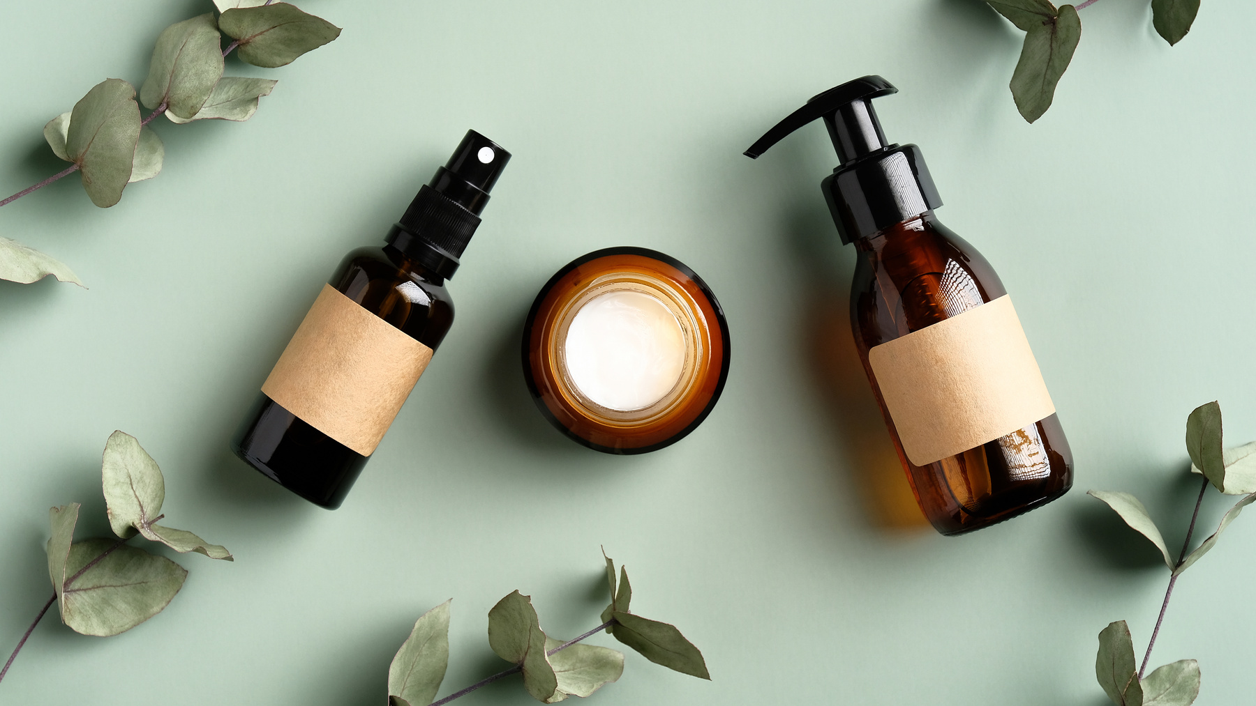 Herbal Skincare Cosmetics Set and Eucalyptus Leaves on Green Background. Amber Glass Body Spray Bottle, Liquid Soap Dispenser, Moisturizer Cream Jar. SPA Natural Organic Beauty Products Design.