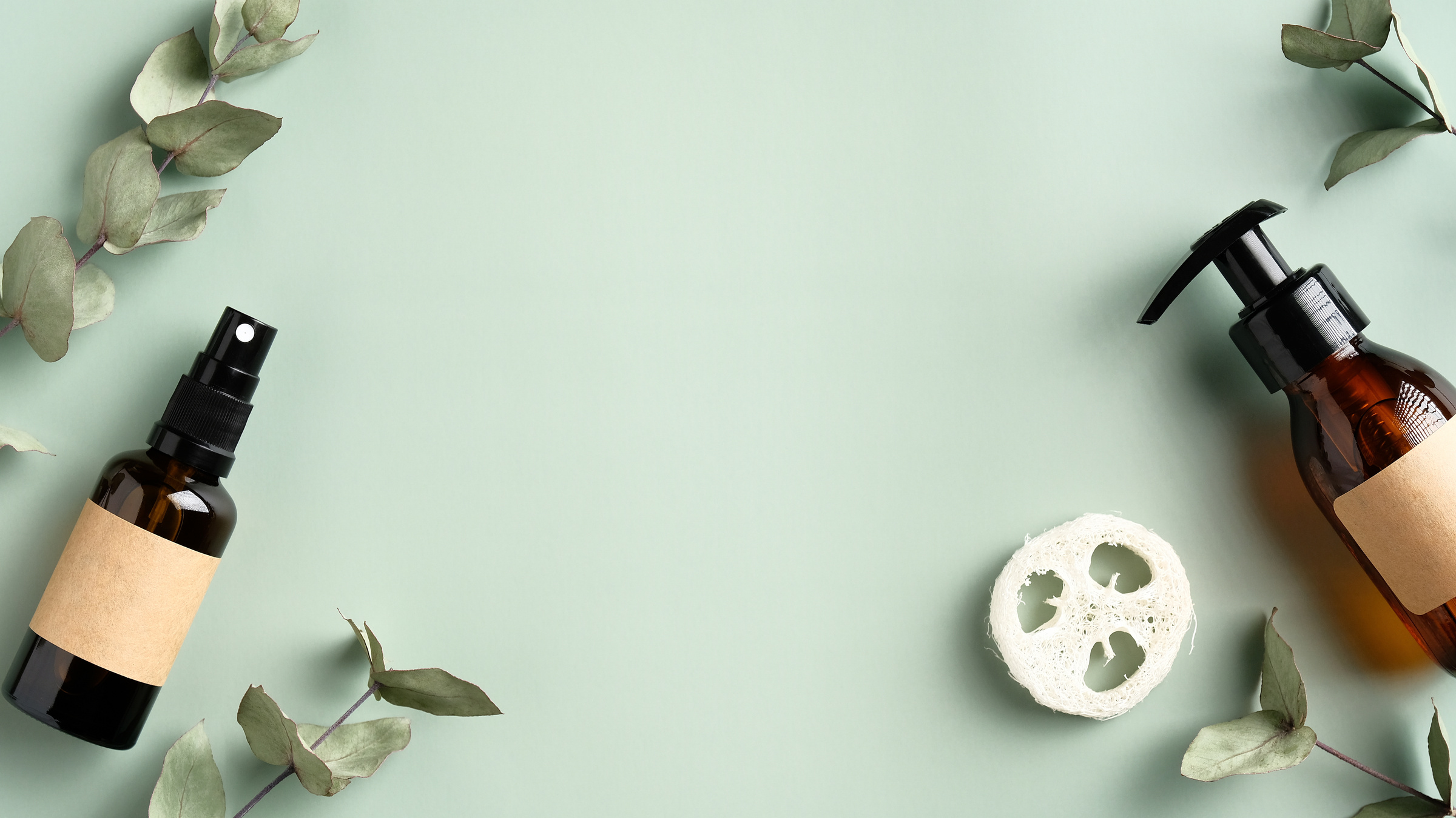 Beauty Salon Banner Mockup. Frame Made of Amber Glass Cosmetics Bottles, Loofah, Eucalyptus Leaves on Green Background. SPA Natural Organic Beauty Products Flat Lay.